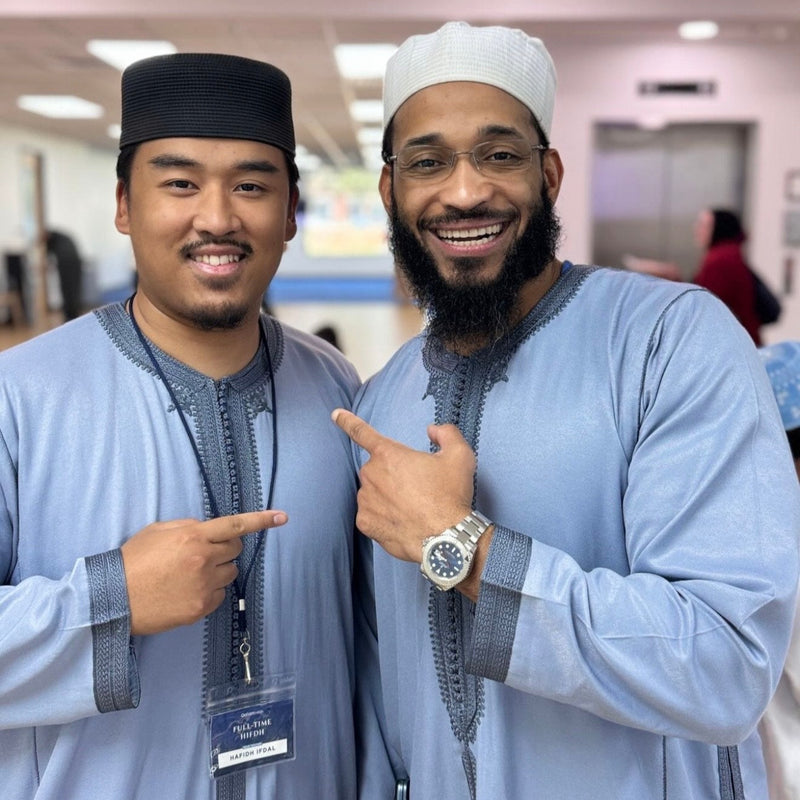 Two men smiling, wearing pastel blue and navy embroidered Moroccan thobes