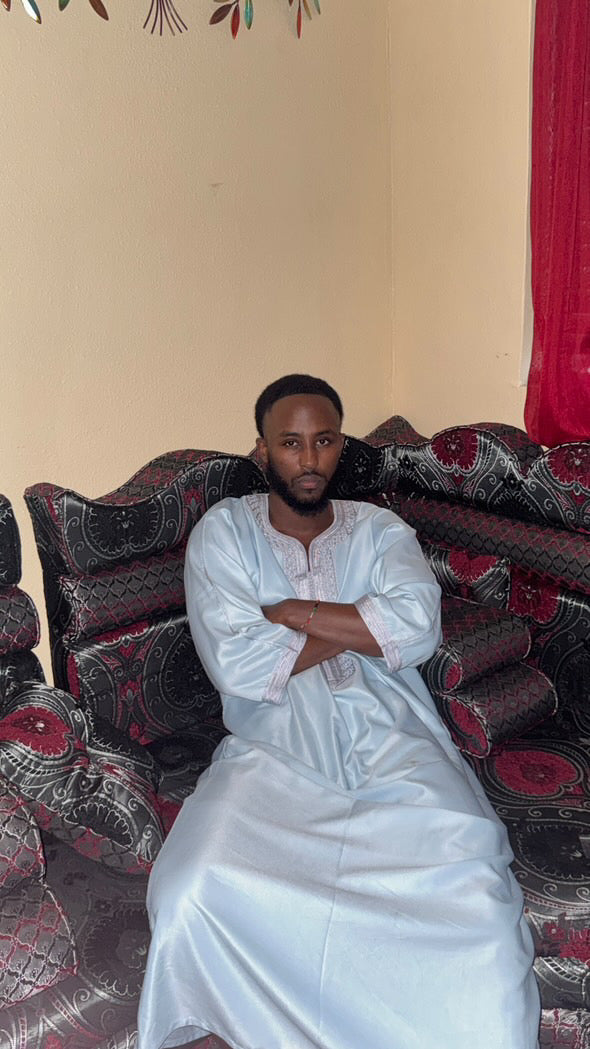 Man seated on a patterned sofa wearing a white Moroccan thobe