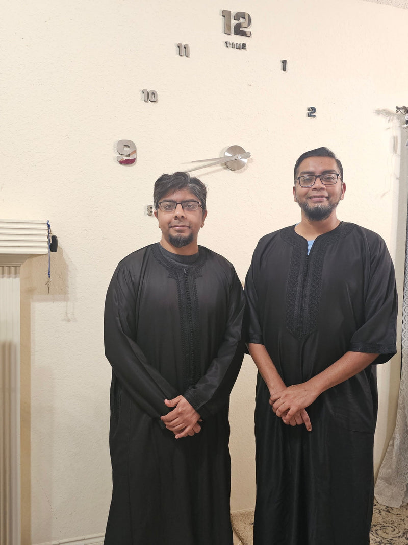Two men wearing black Moroccan thobes indoors