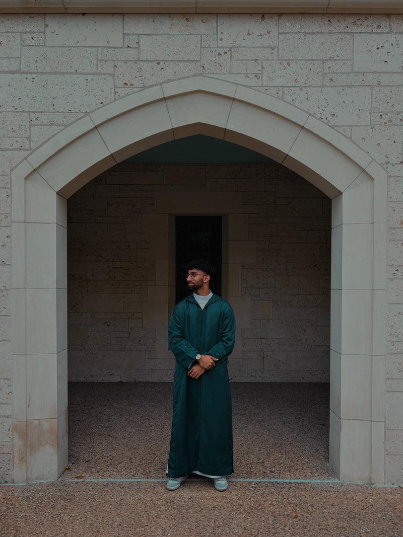 Man in a deep green Moroccan thobe standing in a stone archway