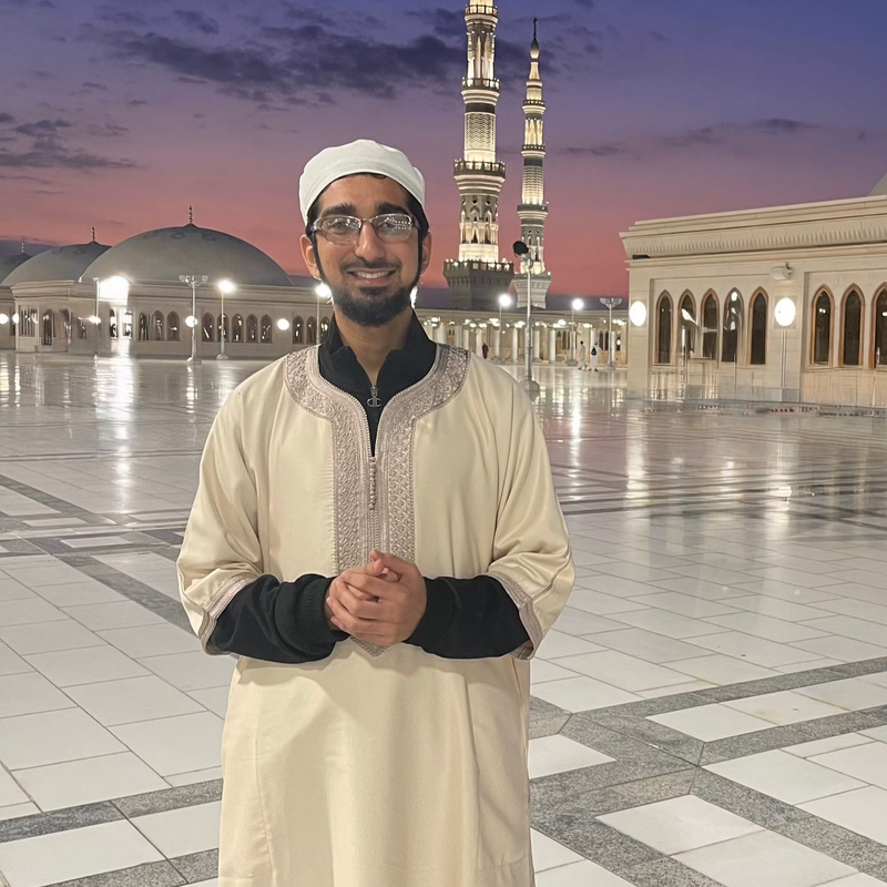 Man in a cream Moroccan thobe standing outside a mosque at dusk