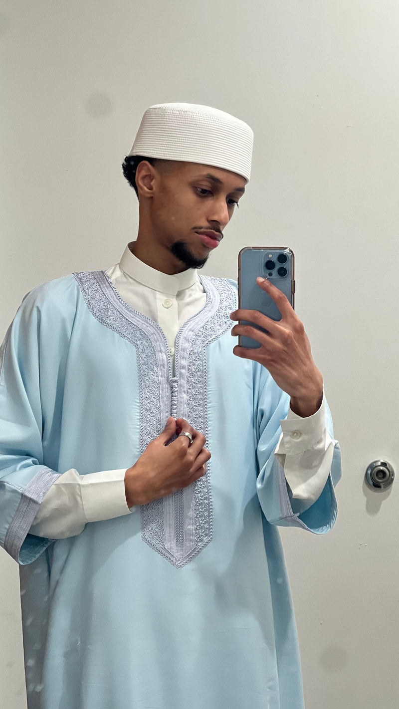 Man in a pastel blue Moroccan thobe and white cap taking a mirror photo